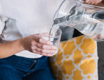 crop-woman-sofa-pouring-water